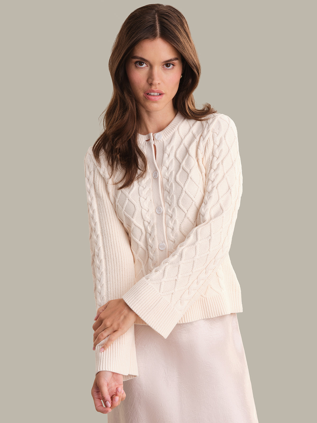 Woman wearing a cream cable knit cardigan against a plain background