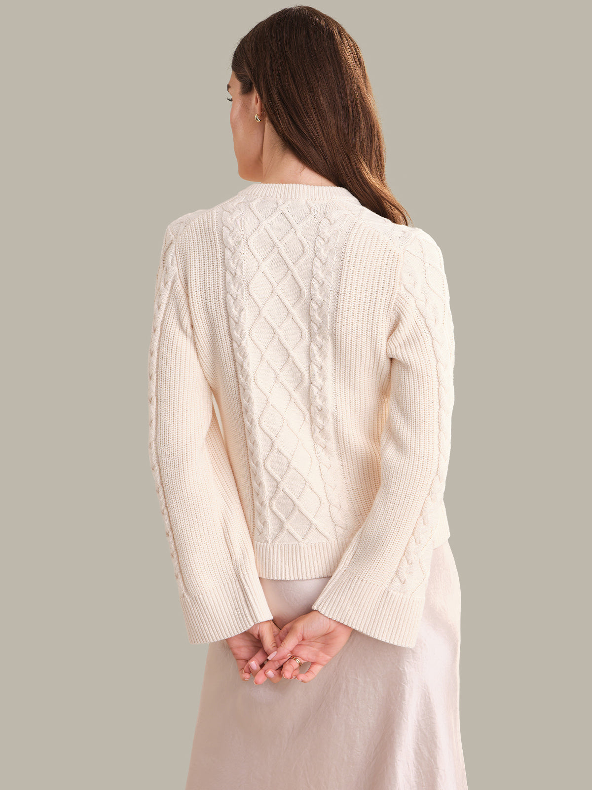 Woman wearing a cream-colored cable knit cardigan against a plain background