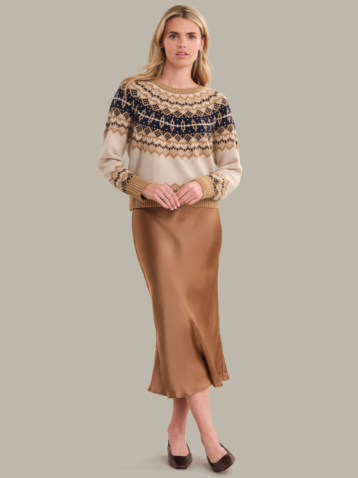 Woman wearing a patterned sweater and brown skirt on a gray background