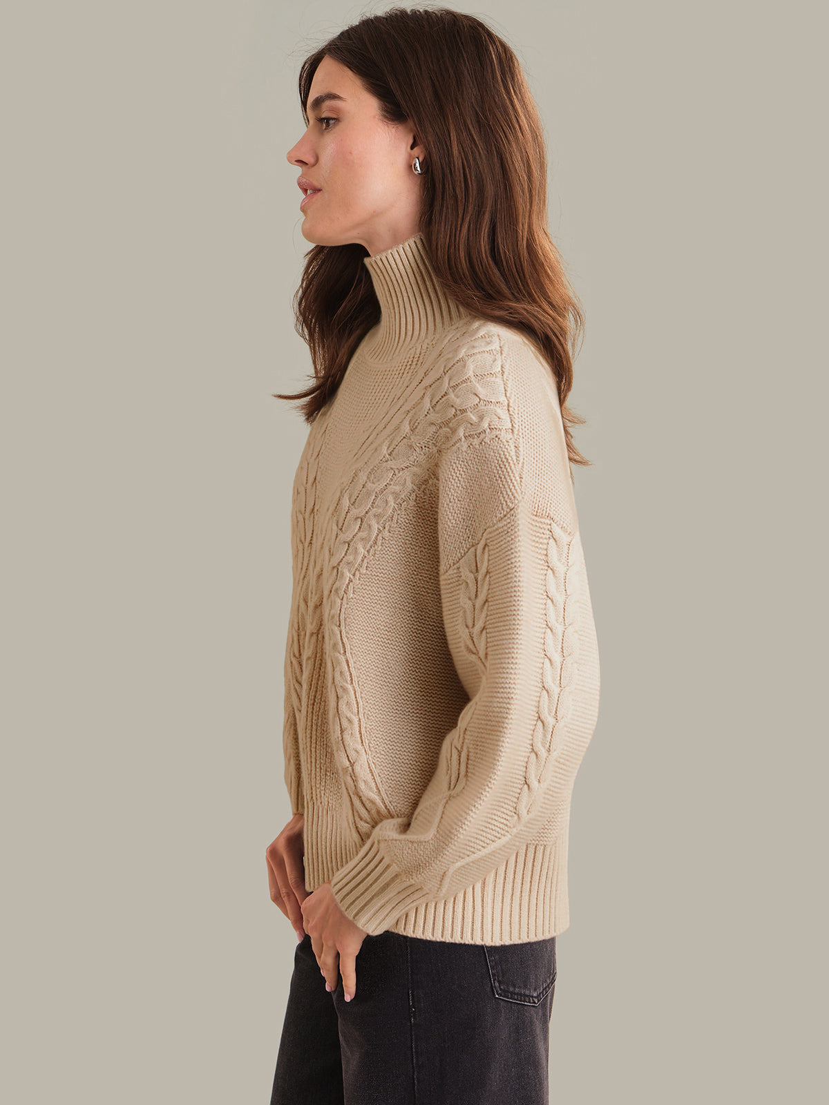 Woman wearing a beige cable knit sweater against a plain background