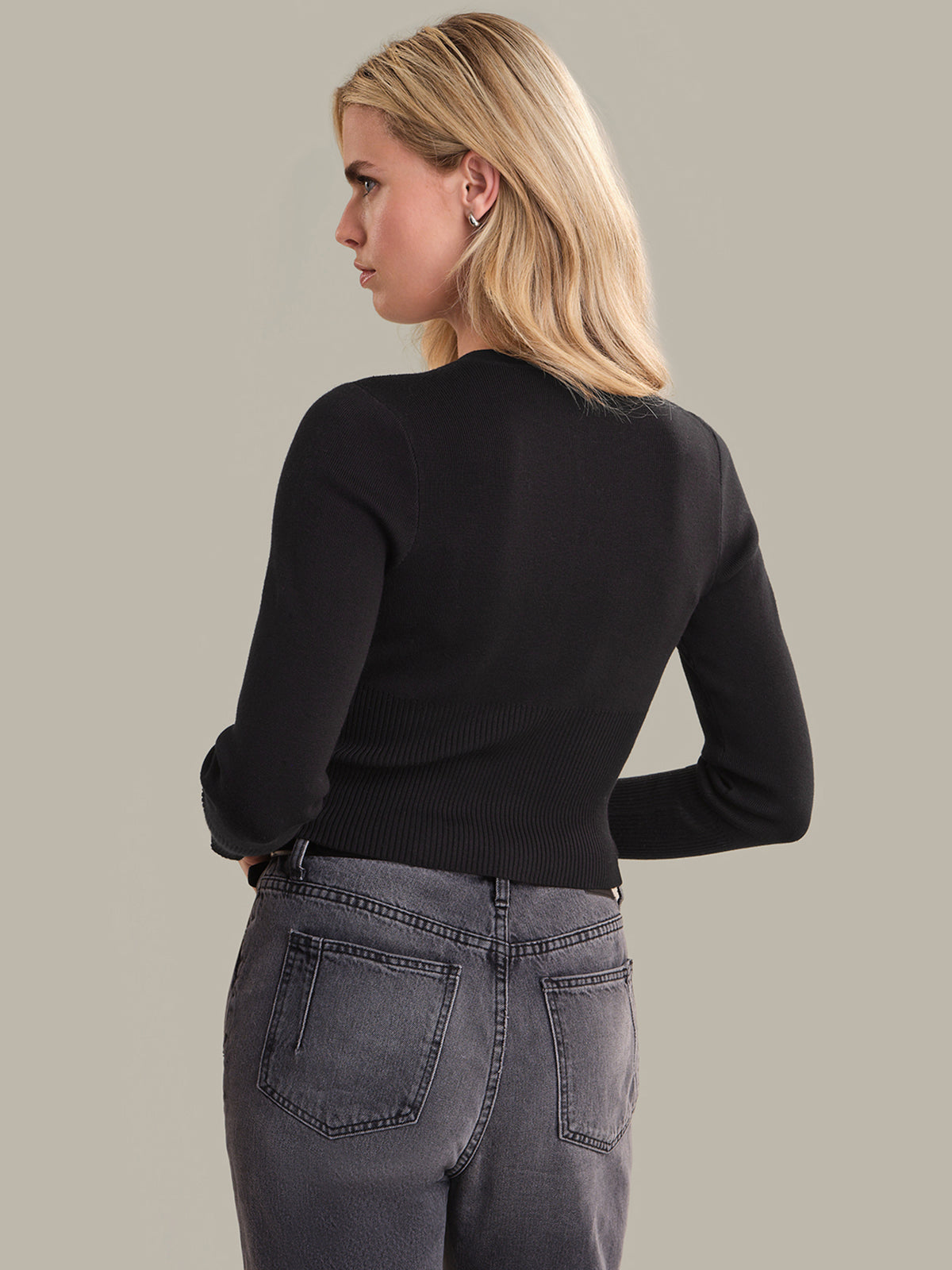 Woman wearing a black sweater and gray jeans against a plain background
