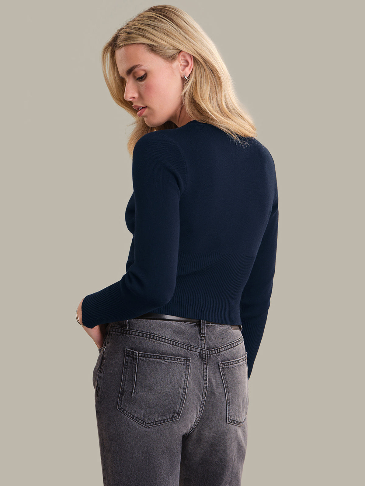 Woman wearing a navy sweater and gray jeans against a beige background