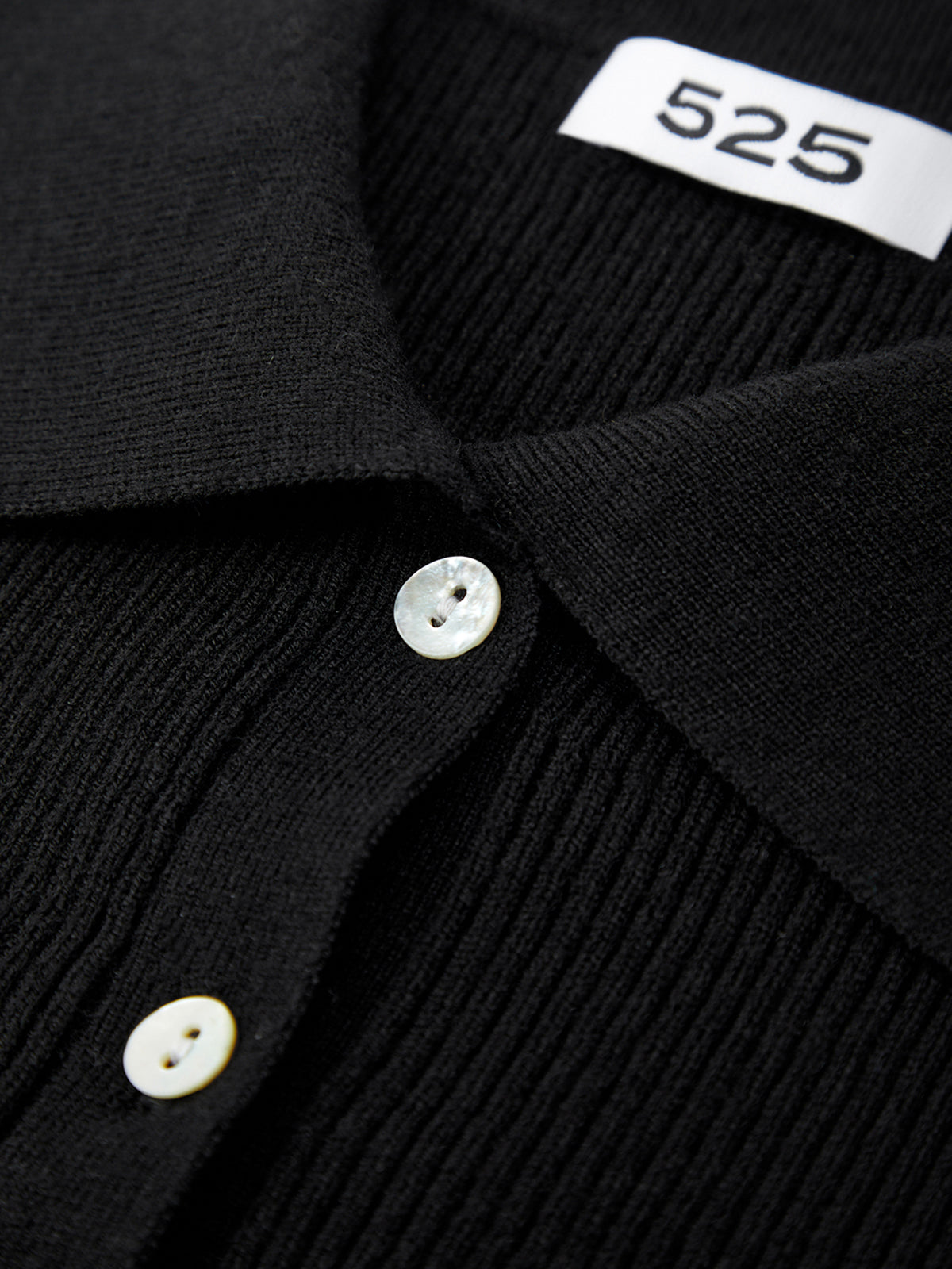 Close-up of a black garment with buttons and a visible brand label.