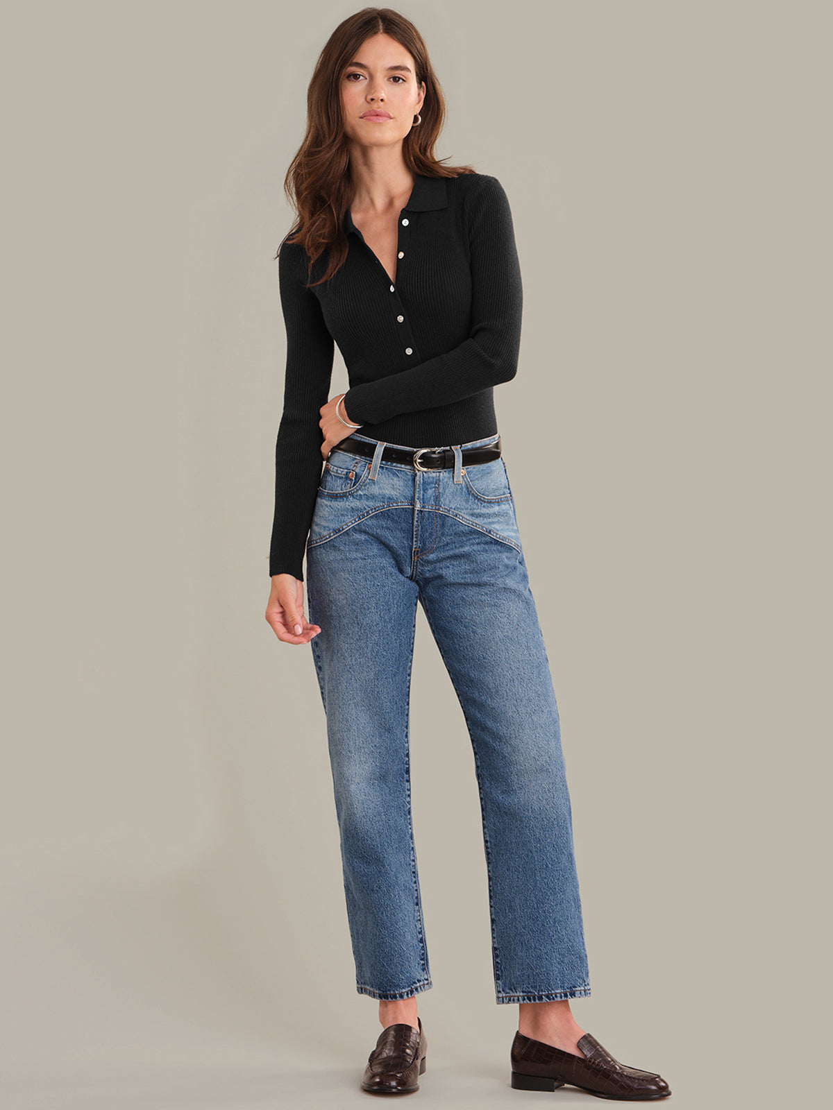 Woman wearing a black long-sleeve shirt and blue jeans on a gray background