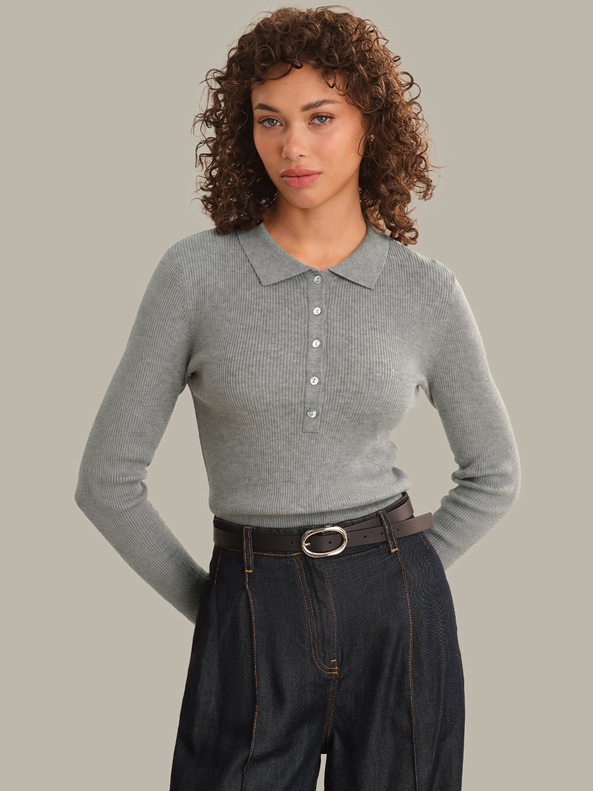 Woman wearing a gray long-sleeve polo shirt and dark jeans on a plain background