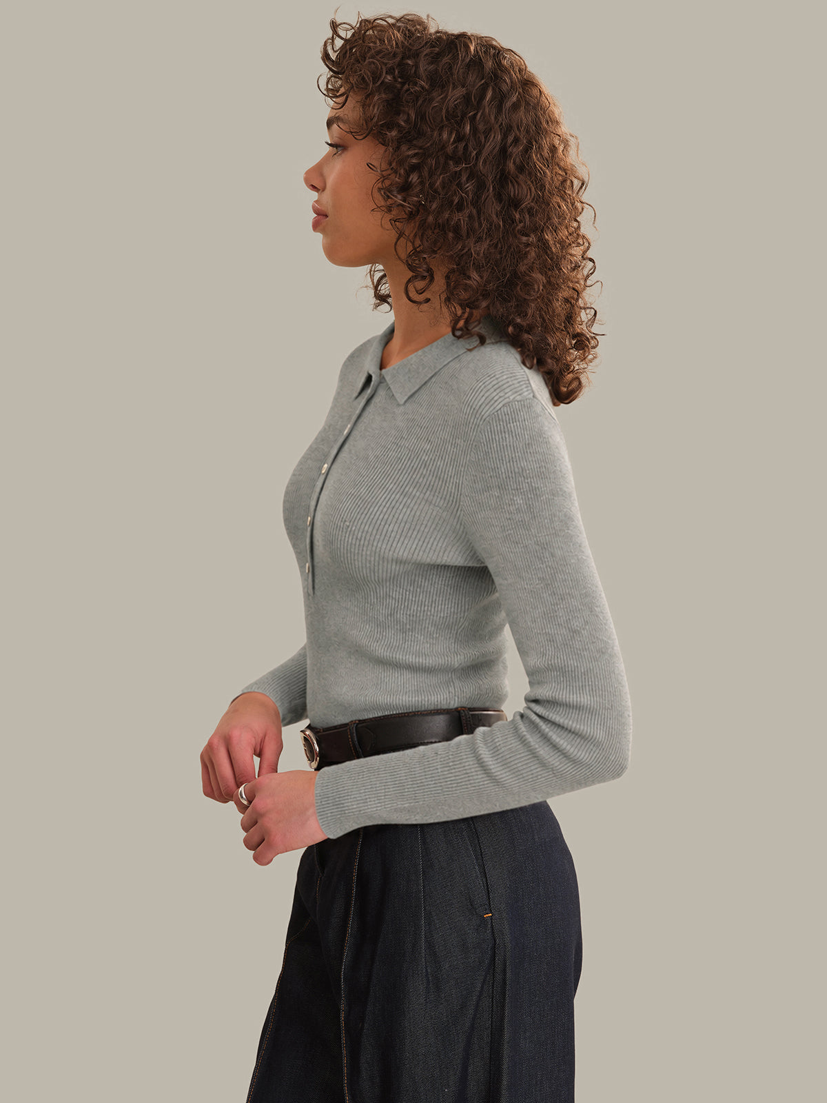 Woman wearing a gray sweater and dark pants against a plain background