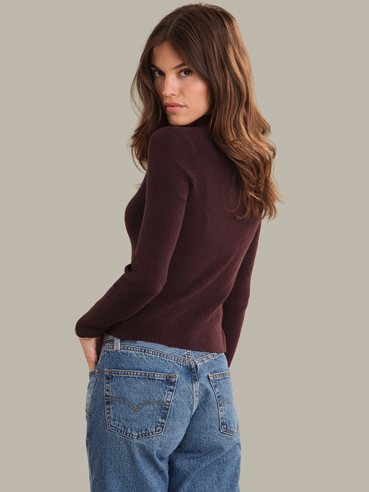 Woman wearing a wine red sweater and blue jeans against a plain background