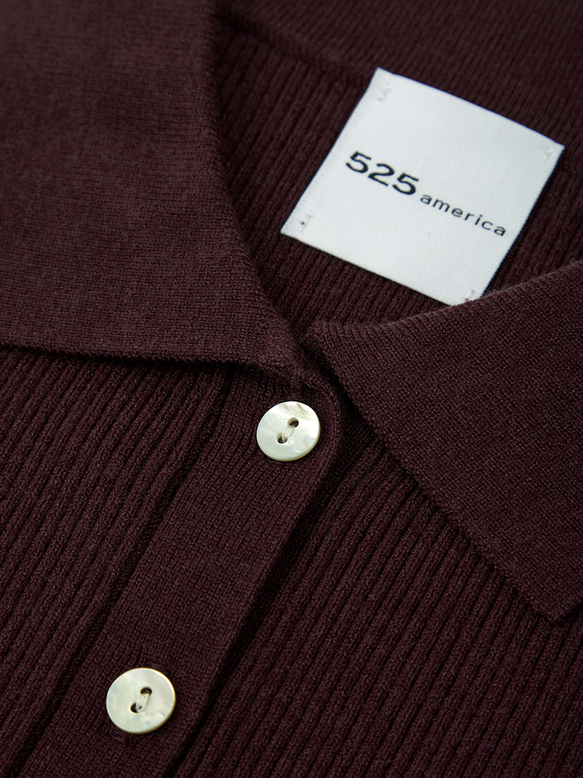 Close-up of a wine red ribbed sweater with buttons and a visible brand label.