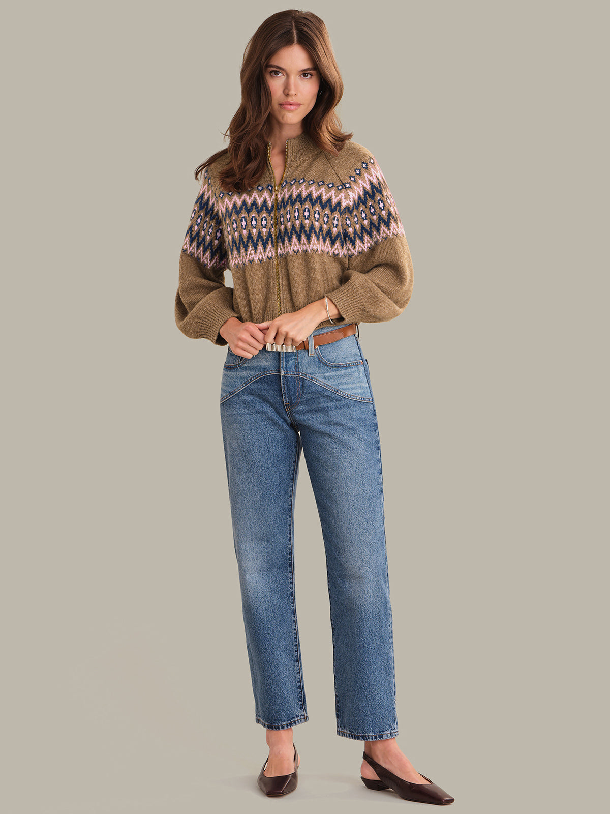 Woman wearing a patterned sweater jacket and blue jeans on a gray background