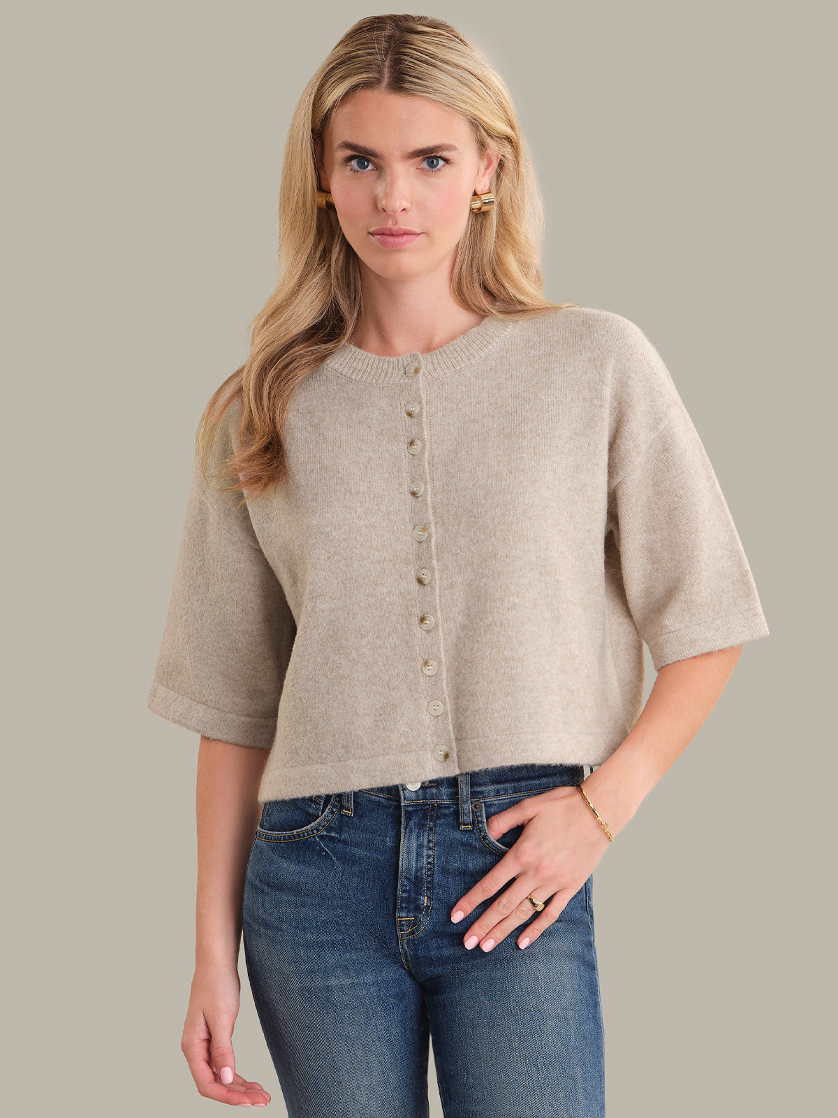 Woman wearing a beige short-sleeve cardigan and blue jeans on a gray background