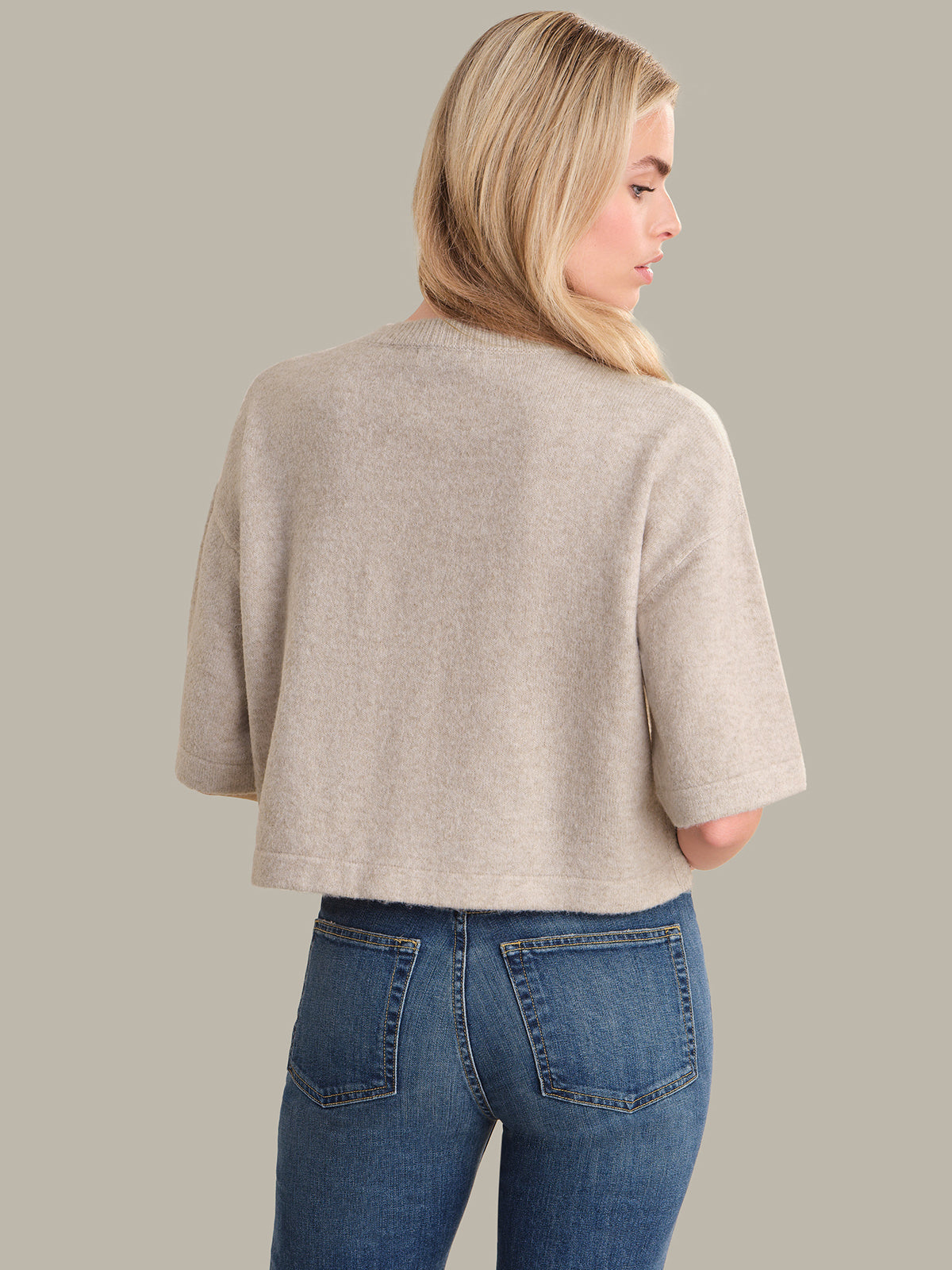 Woman wearing a beige cardigan and blue jeans on a gray background