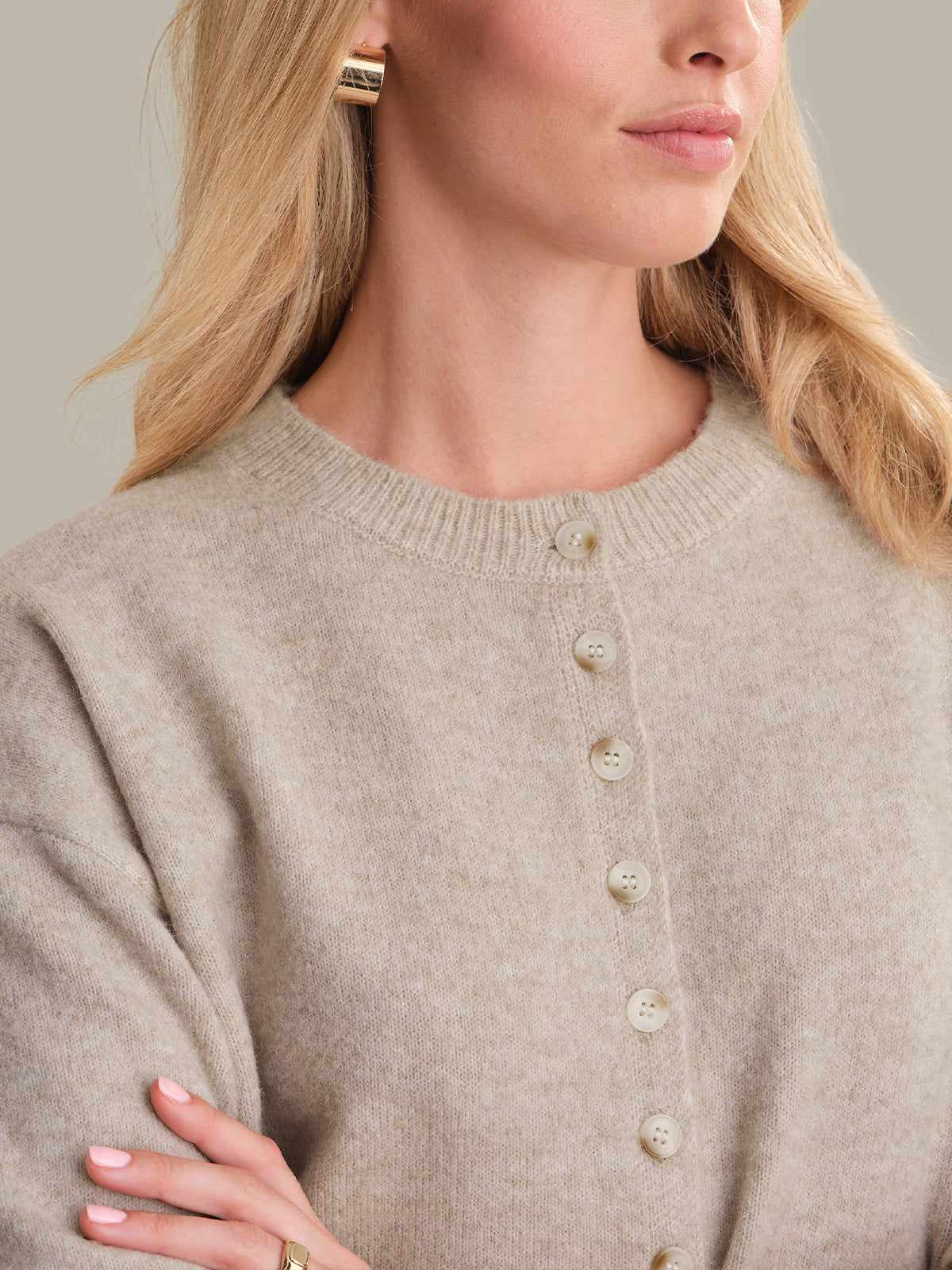 Close-up of a person wearing a beige cardigan with a neutral background