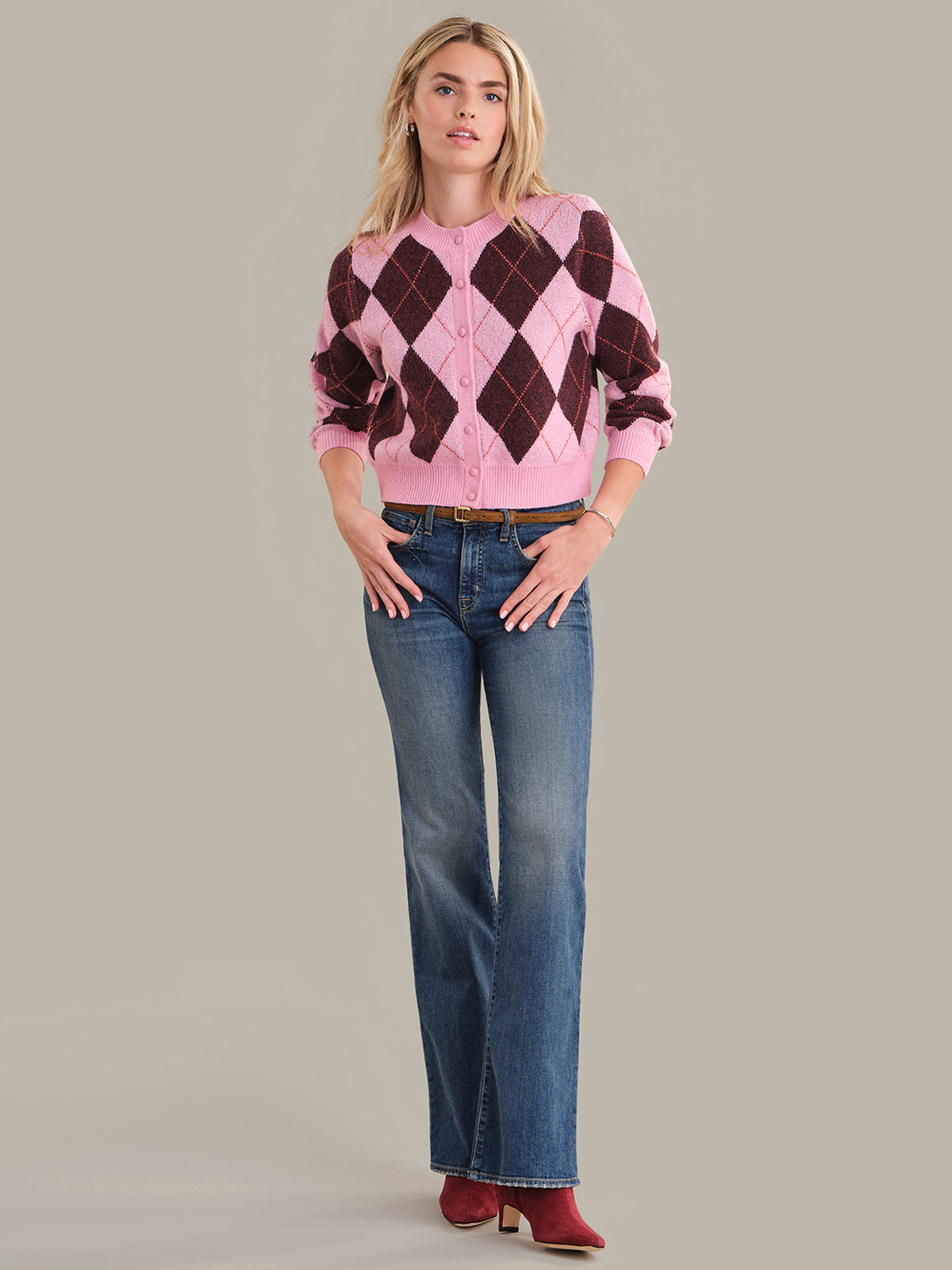 Woman wearing a pink and brown argyle sweater with blue jeans on a gray background