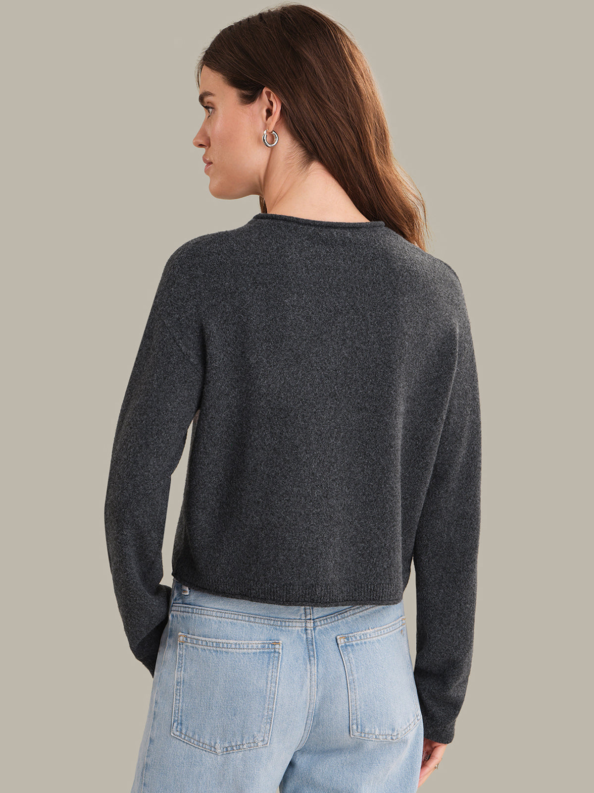 Woman wearing a dark gray sweater and light blue jeans on a beige background