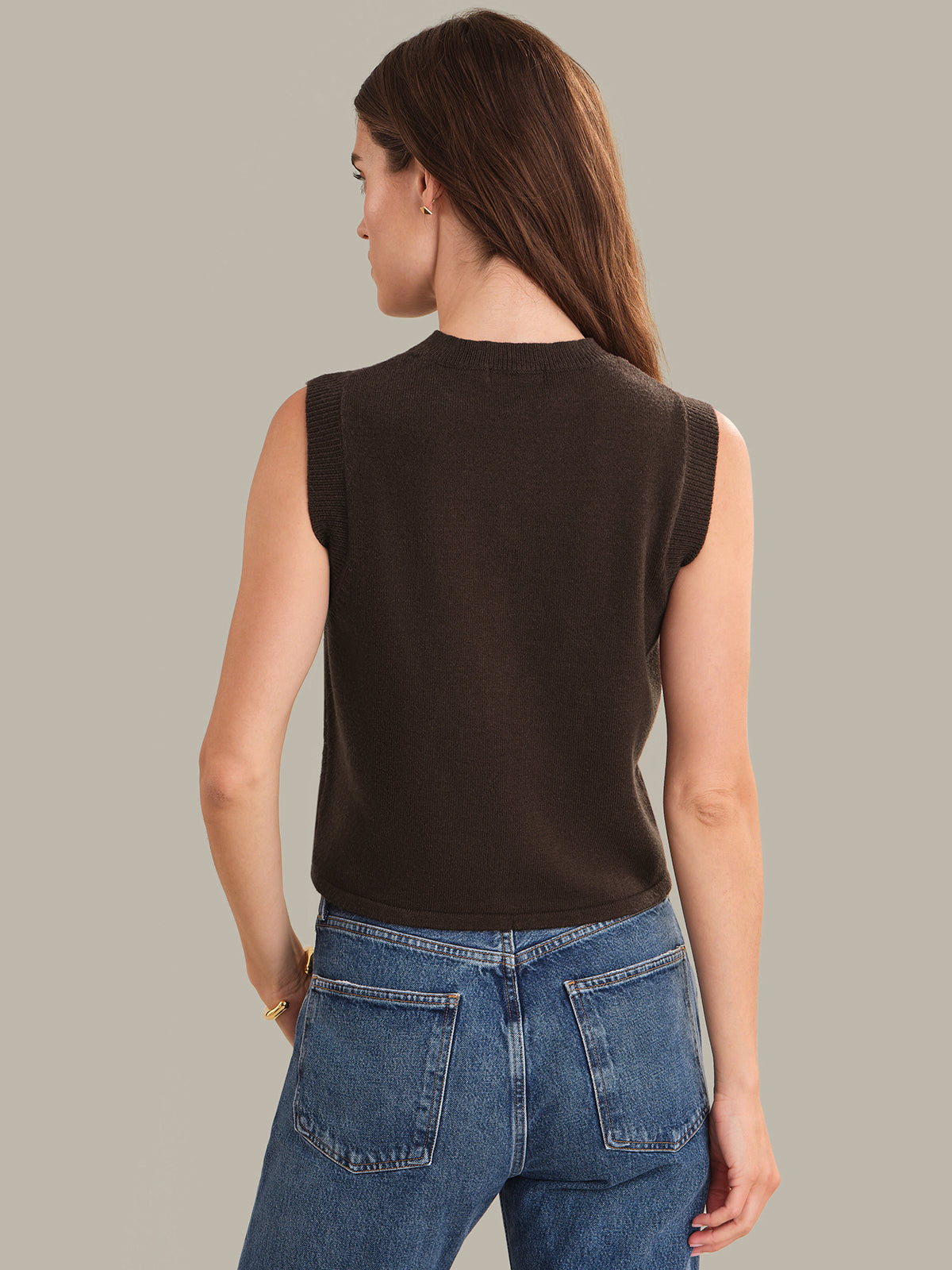 Woman wearing a shaved chocolate sleeveless top and blue jeans against a plain background