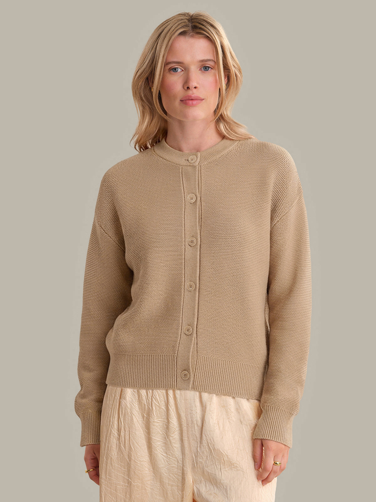 Woman wearing a beige cardigan against a plain background