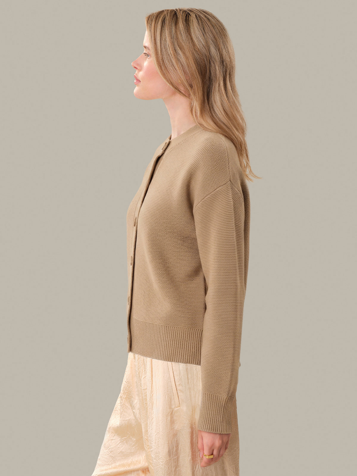 Woman wearing a beige cardigan over a light dress against a neutral background