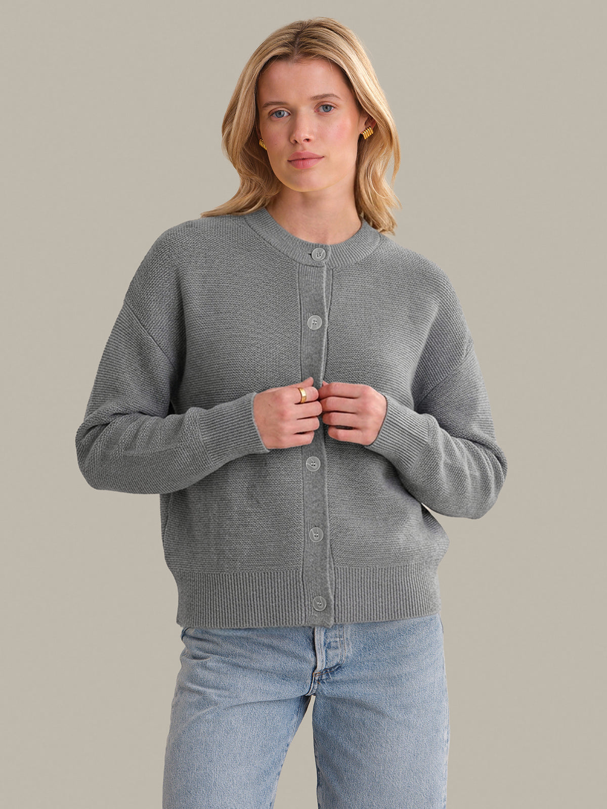 Woman wearing a gray cardigan and light blue jeans against a neutral background