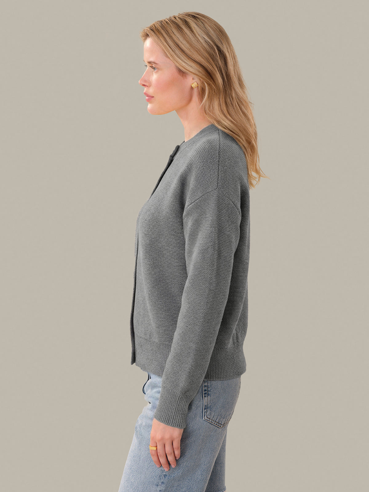 Woman wearing a gray cardigan and light blue jeans against a plain background