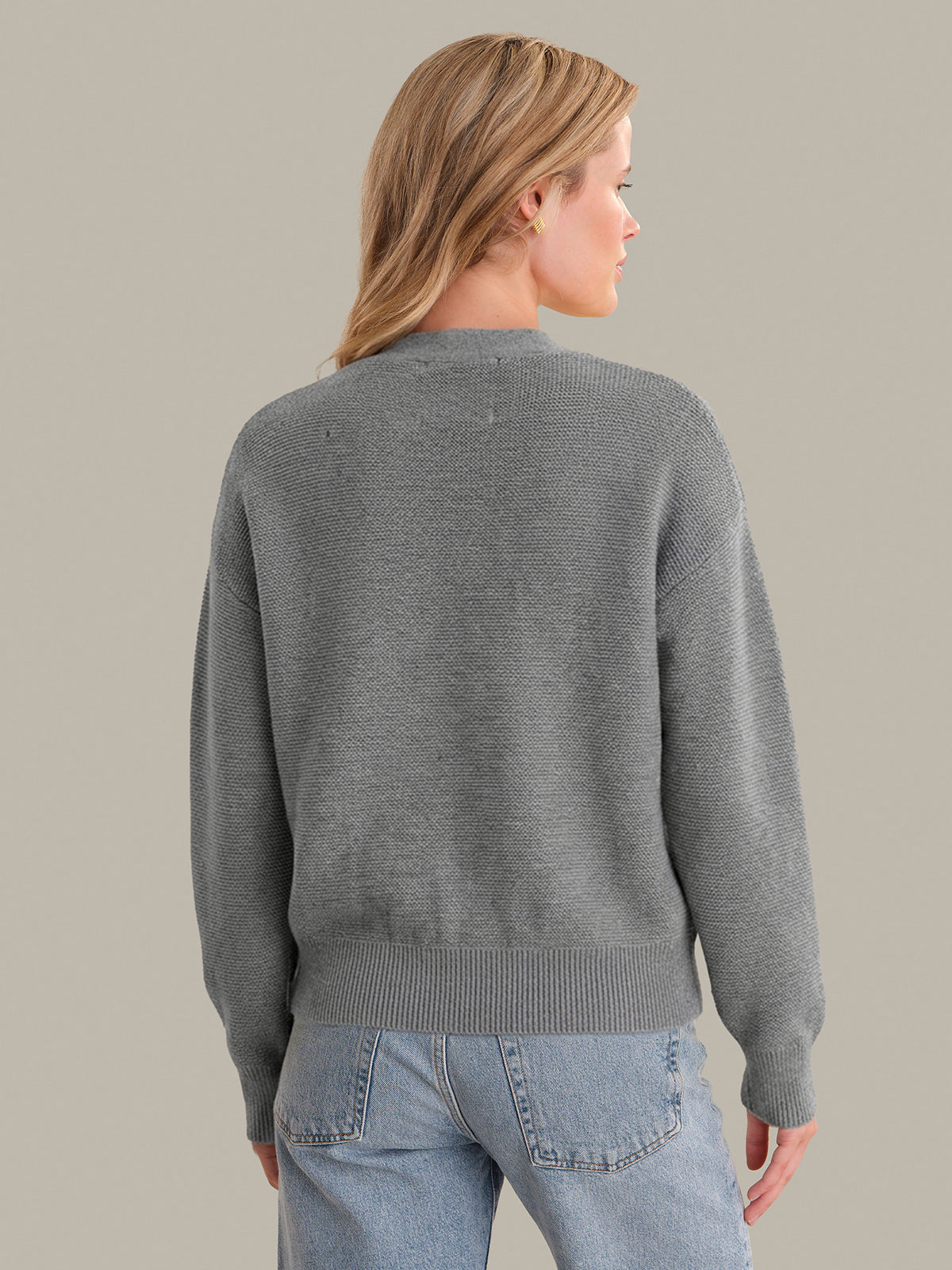 Person wearing a gray sweater and blue jeans against a plain background
