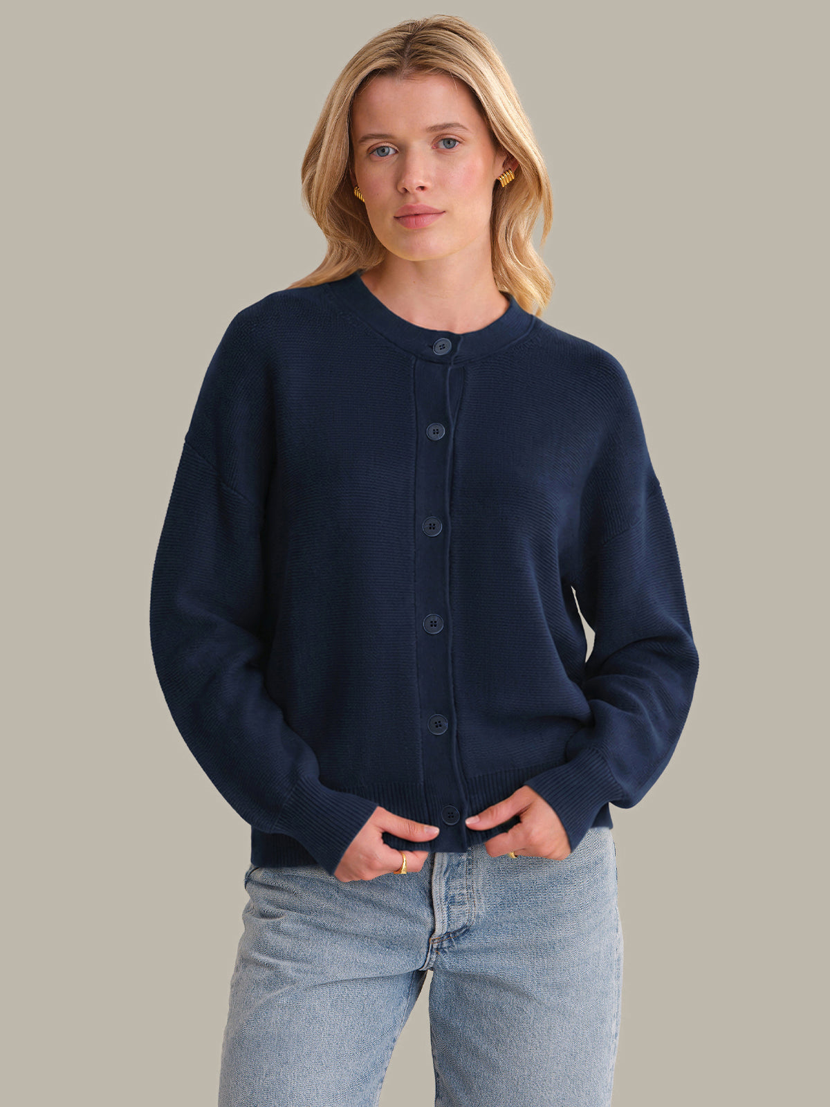 Woman wearing a navy blue cardigan over a white shirt with light blue jeans on a beige background