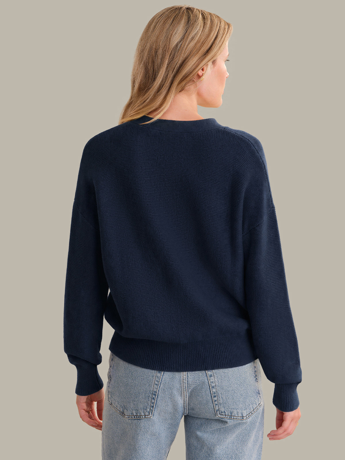 Person wearing a navy cardigan and light blue jeans against a neutral background