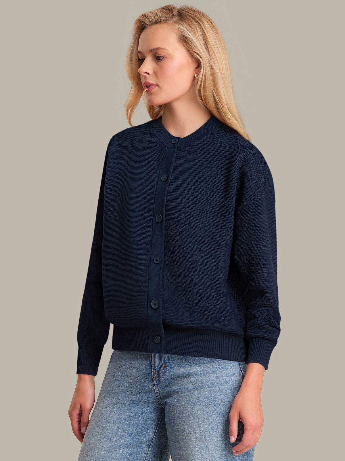 Woman wearing a navy cardigan and blue jeans against a plain background