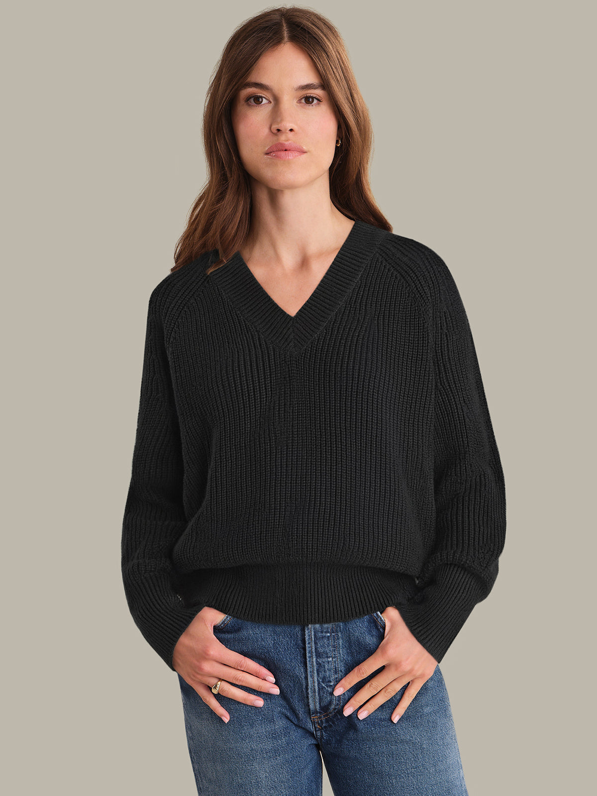 Woman wearing a black sweater and blue jeans against a plain background