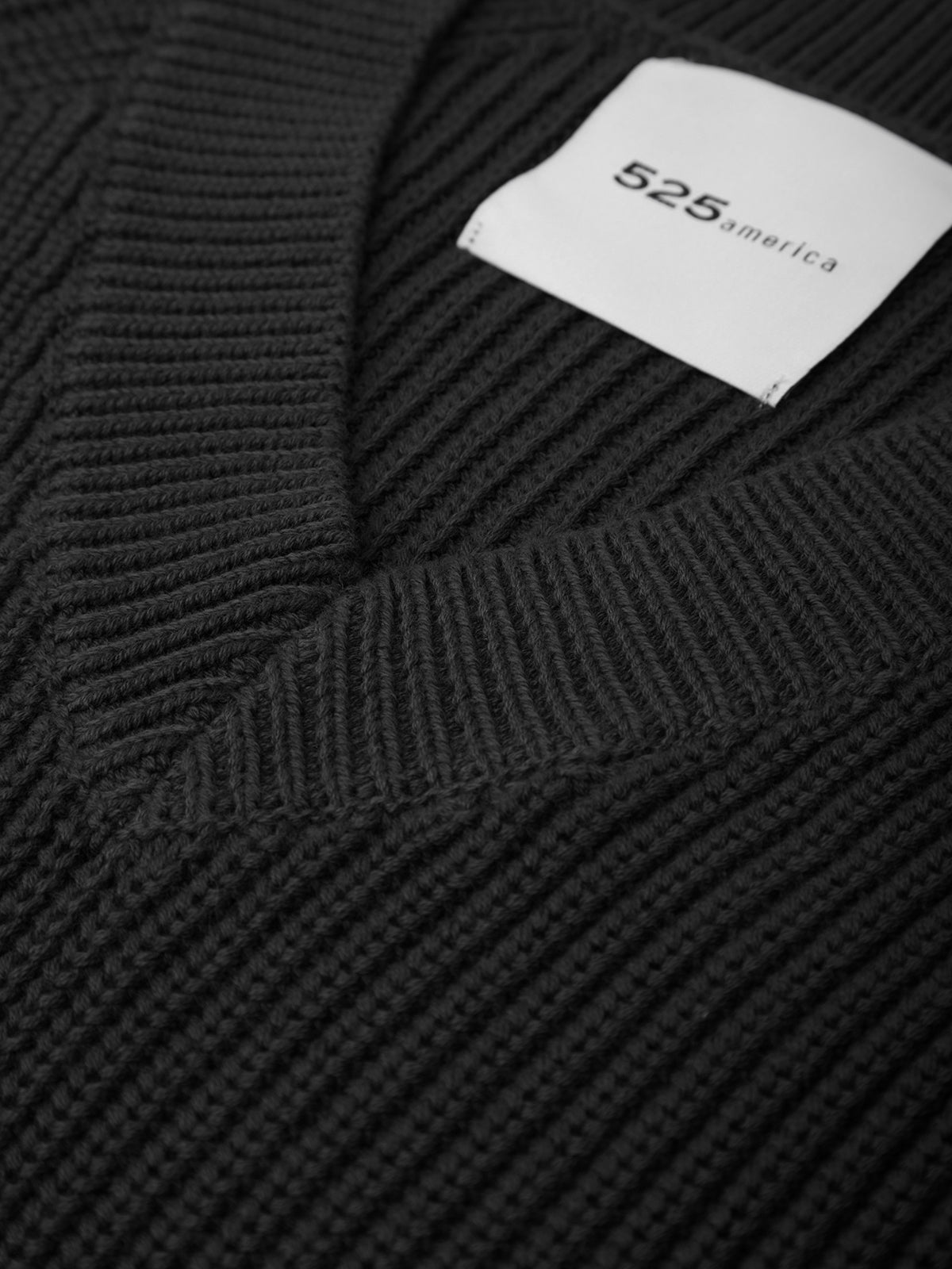 Black ribbed sweater with a visible brand label on a dark background