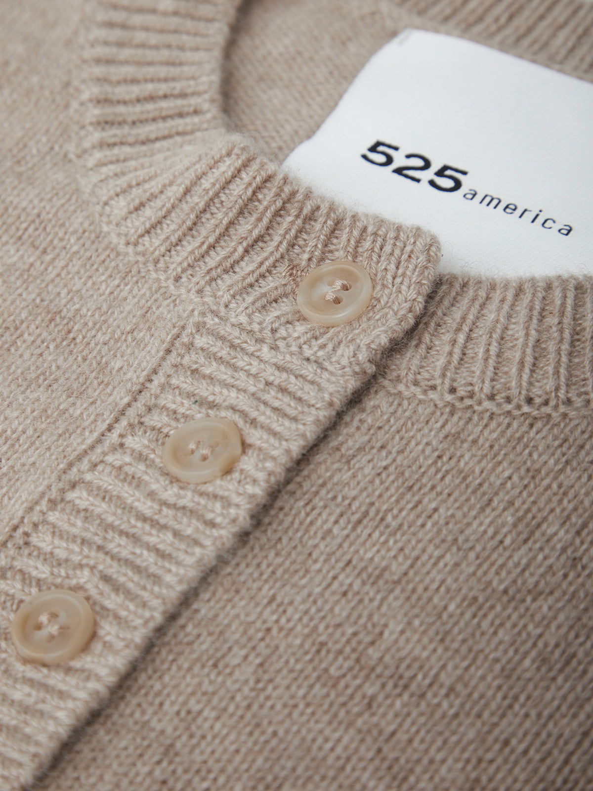 Close-up of a beige sweater with buttons and a visible brand label.