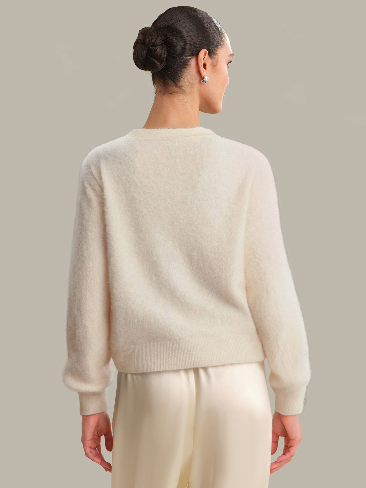 Person wearing a cream-colored sweater and pants against a neutral background