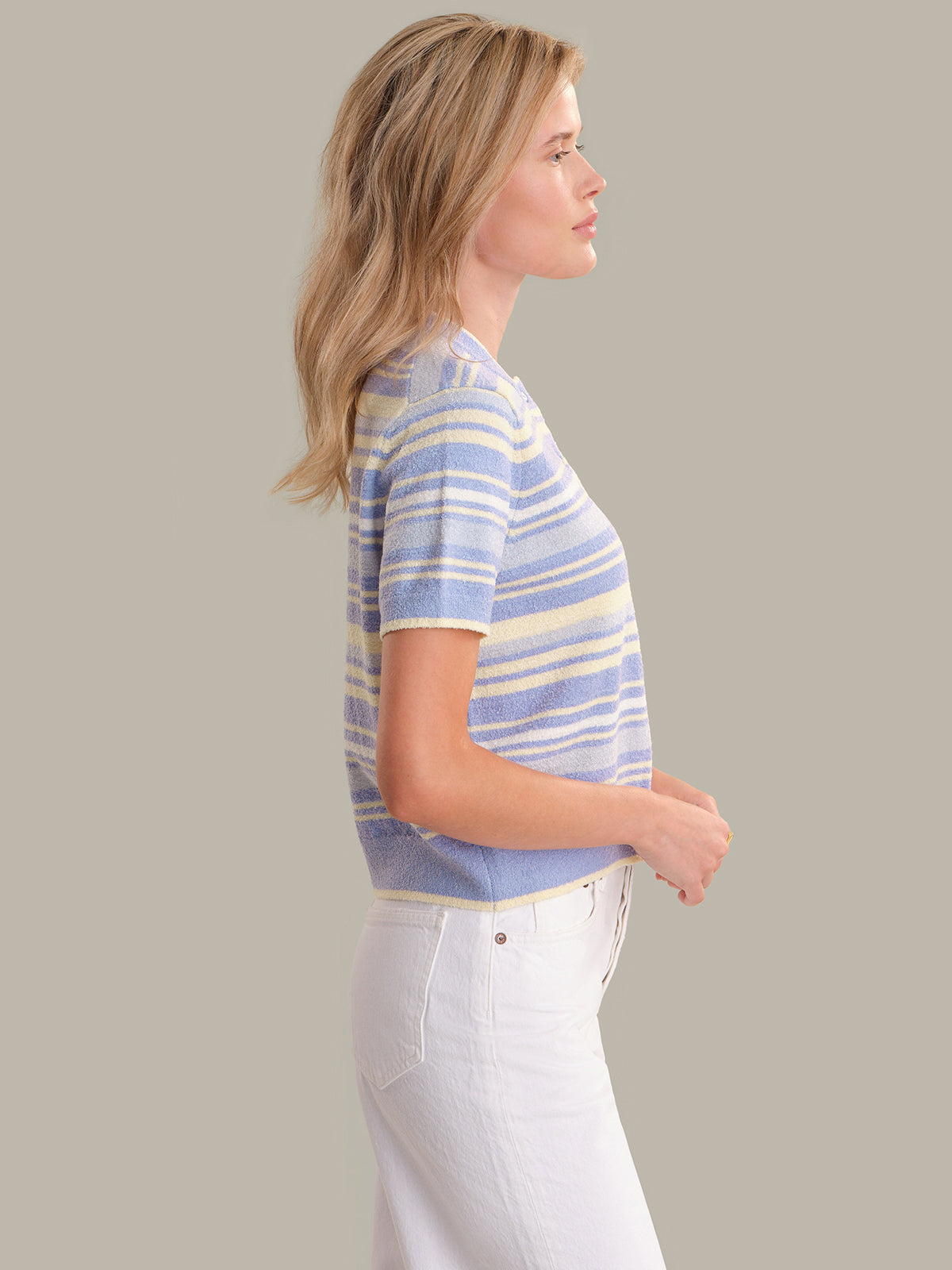 Woman wearing a striped shirt and white pants against a plain background