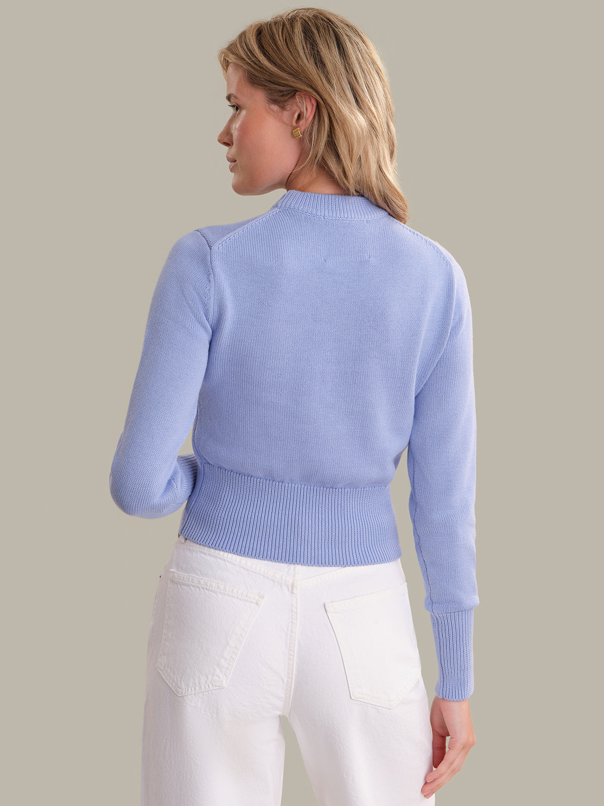 Woman wearing a light blue sweater and white pants on a plain background