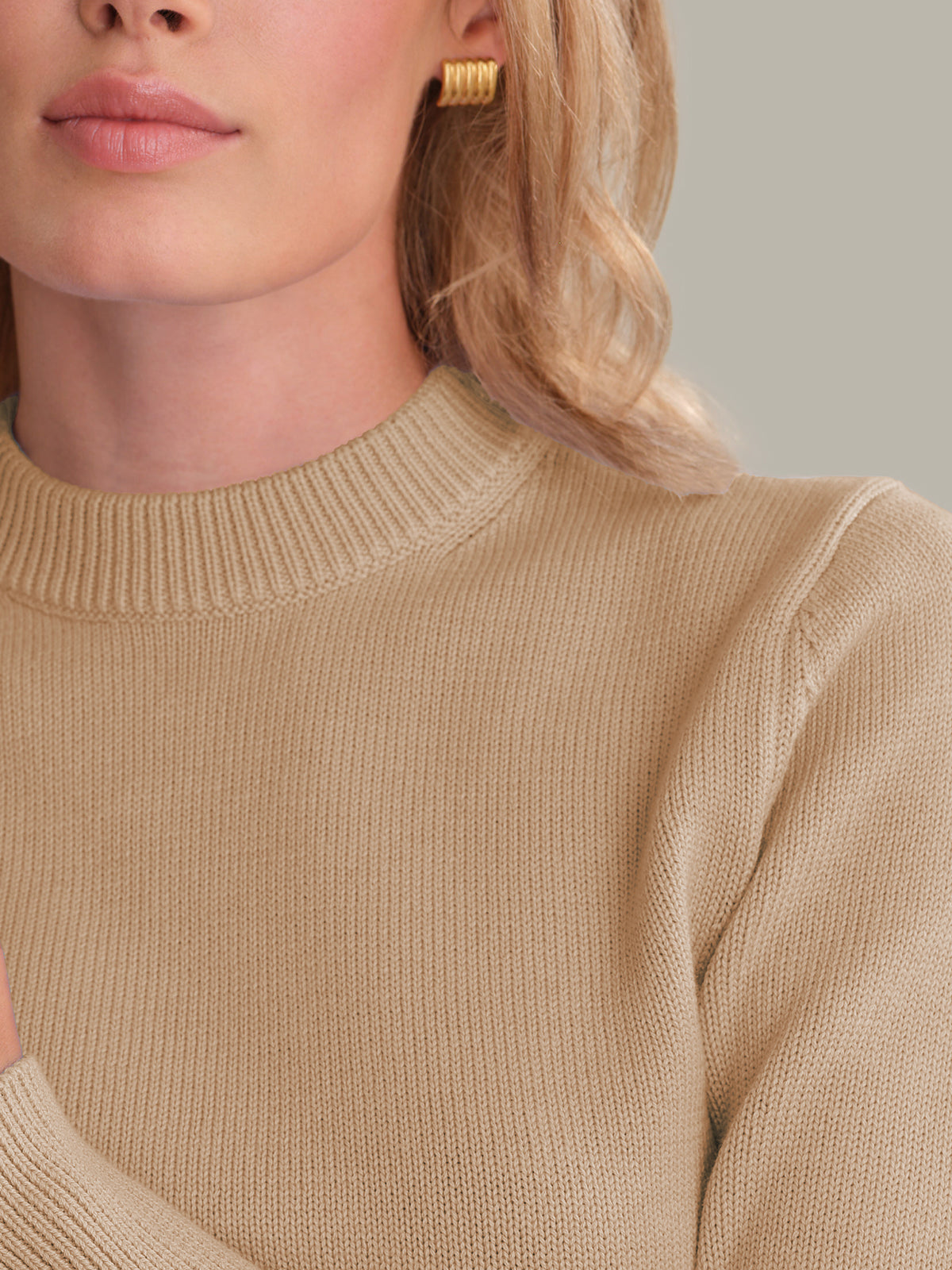 Close-up of a person wearing a beige sweater with a neutral background