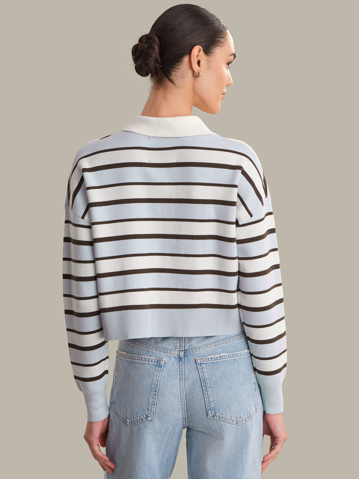 Person wearing a striped sweater and jeans on a plain background