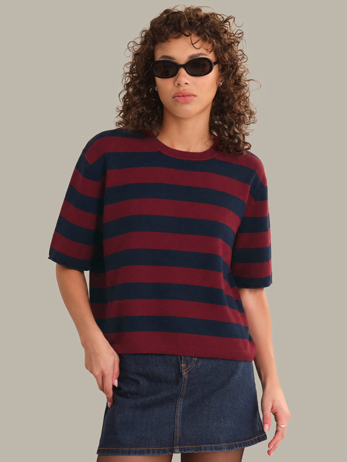 Woman wearing a striped shirt and denim skirt against a plain background