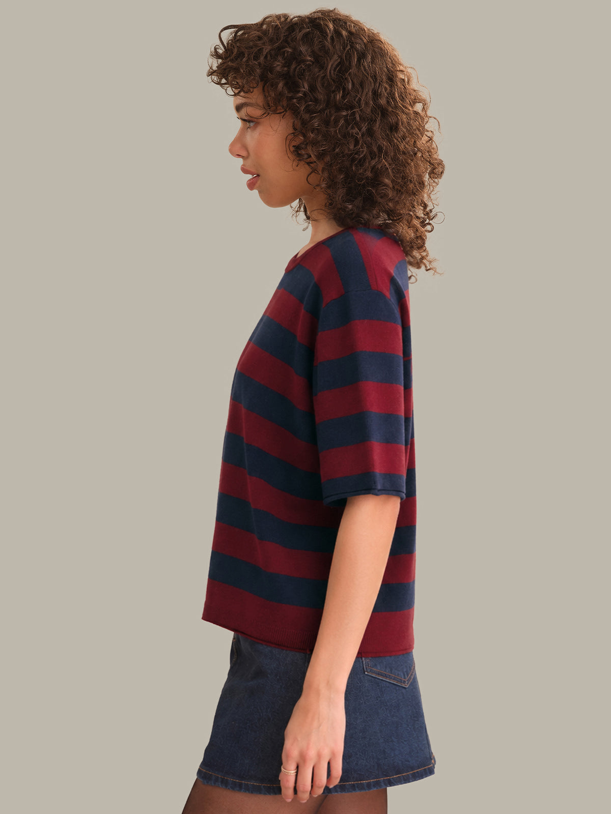 Person wearing a red and navy striped shirt with a denim skirt on a plain background