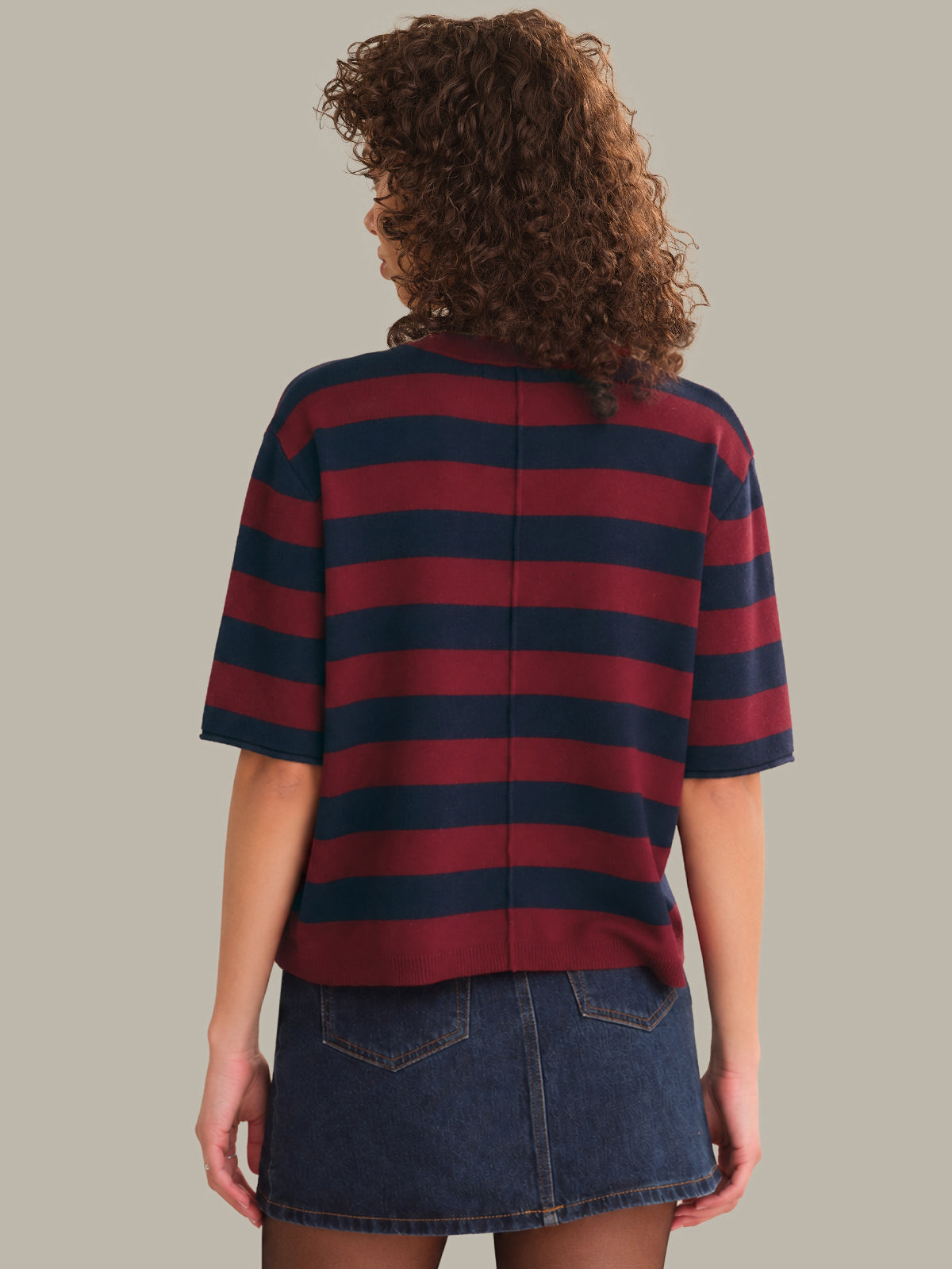 Person wearing a red and navy striped shirt with a denim skirt on a plain background