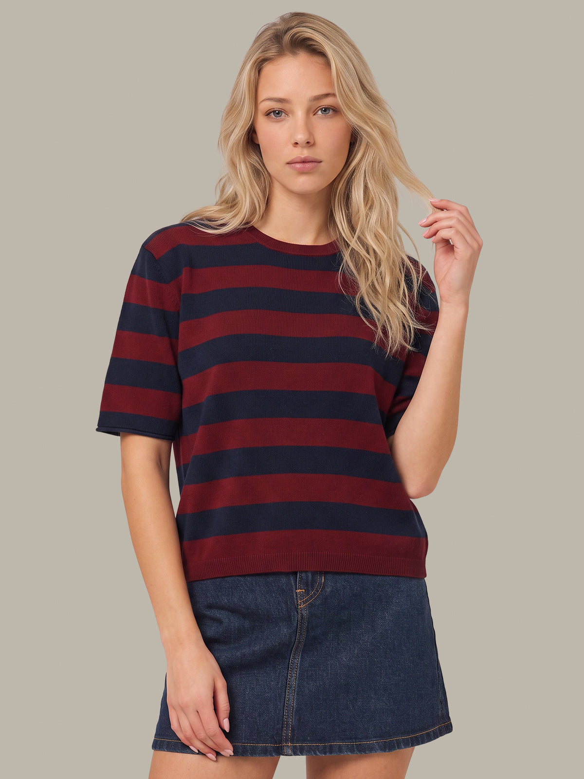 A blonde woman wearing a short-sleeve crewneck t-shirt with horizontal burgundy and navy stripes, paired with a dark blue denim mini skirt, set against a solid light gray background.