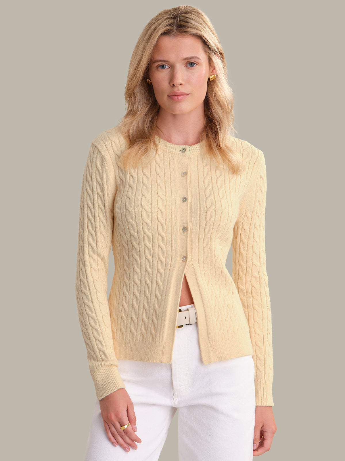 Woman wearing a light yellow cable knit cardigan over a white top on a neutral background