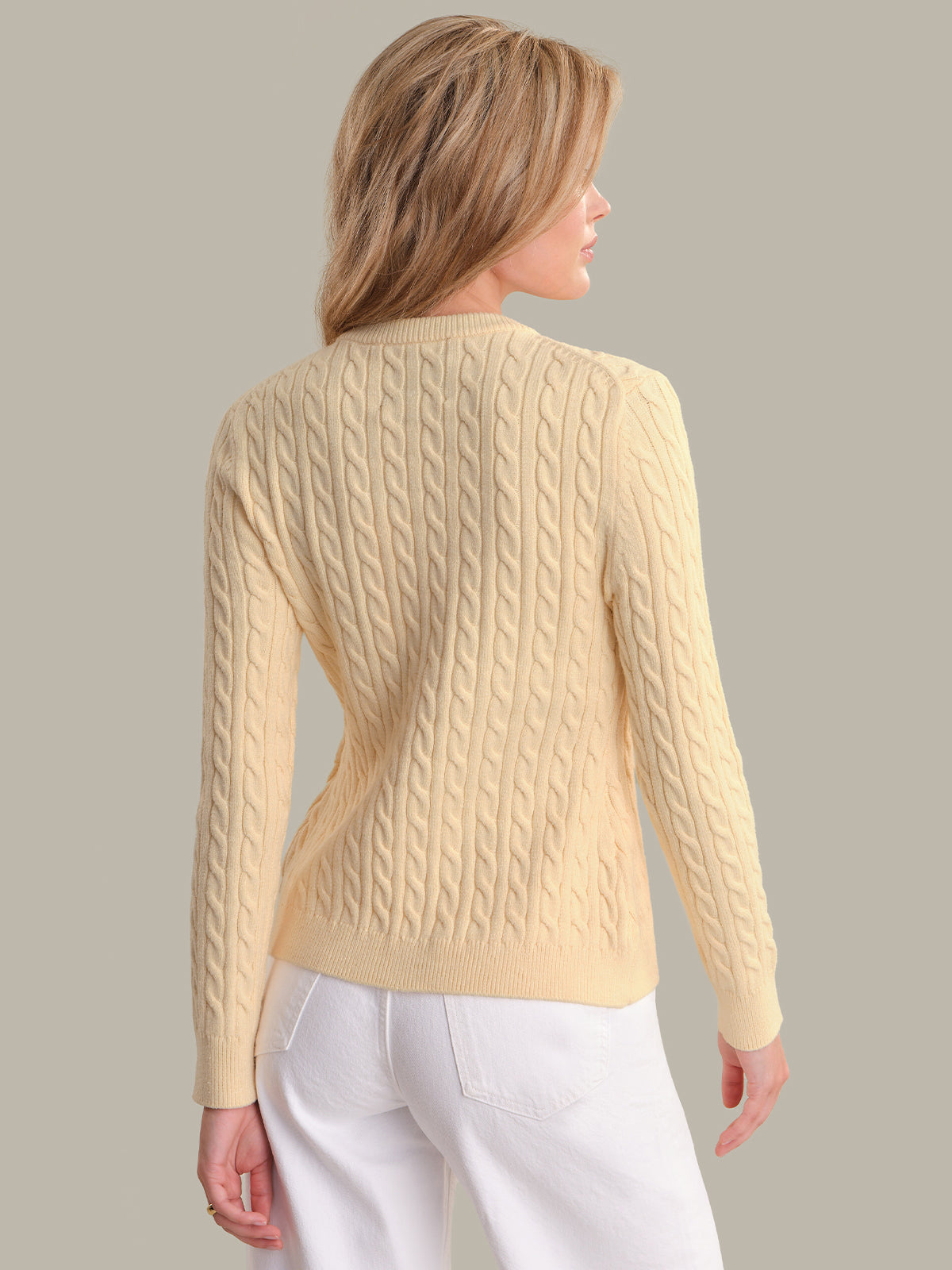 Woman wearing a light yellow cable knit sweater against a plain background