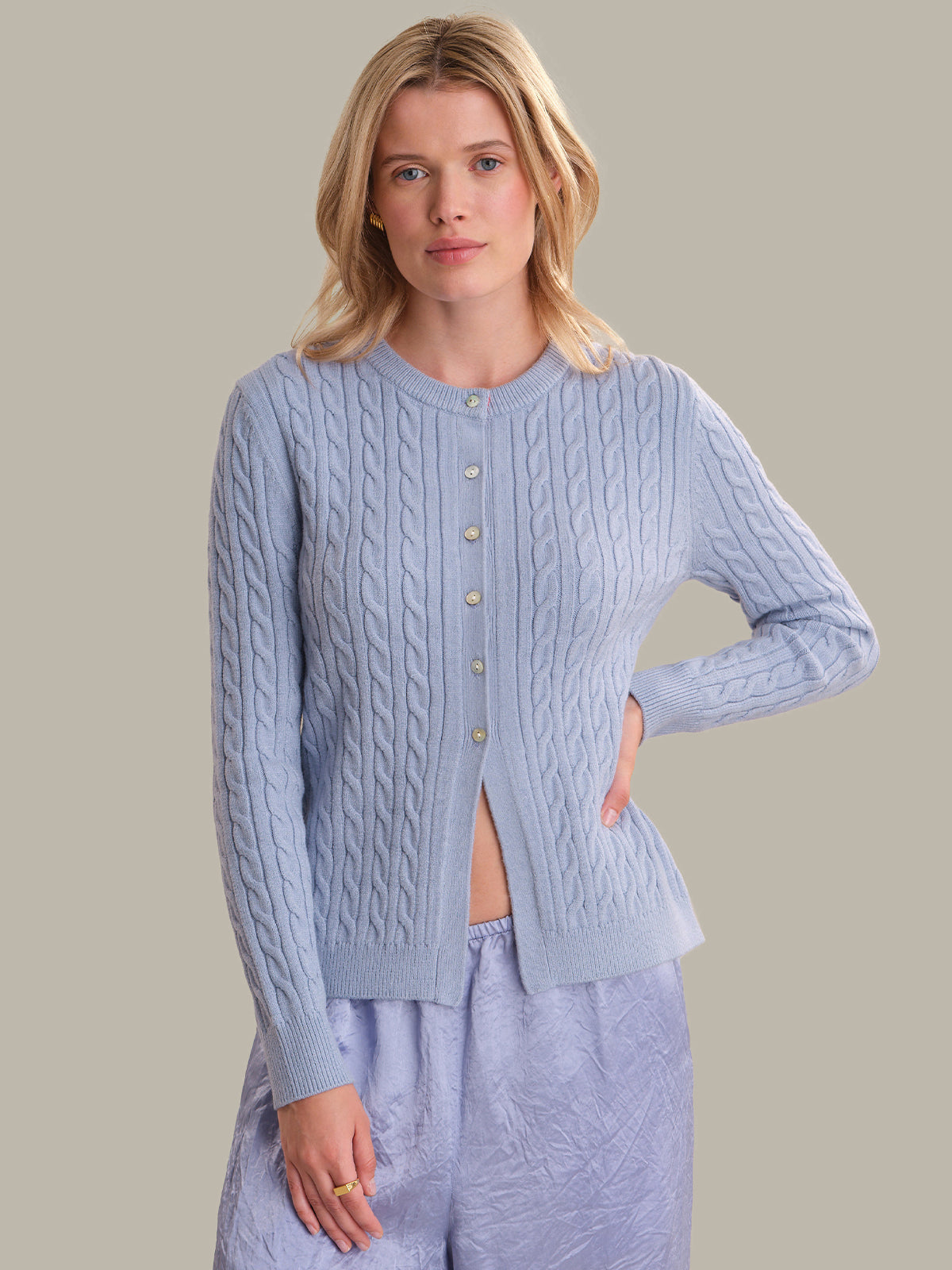 A woman modeling a light blue cable-knit cardigan with gold buttons, paired with matching light blue textured pajama pants, against a solid beige background.