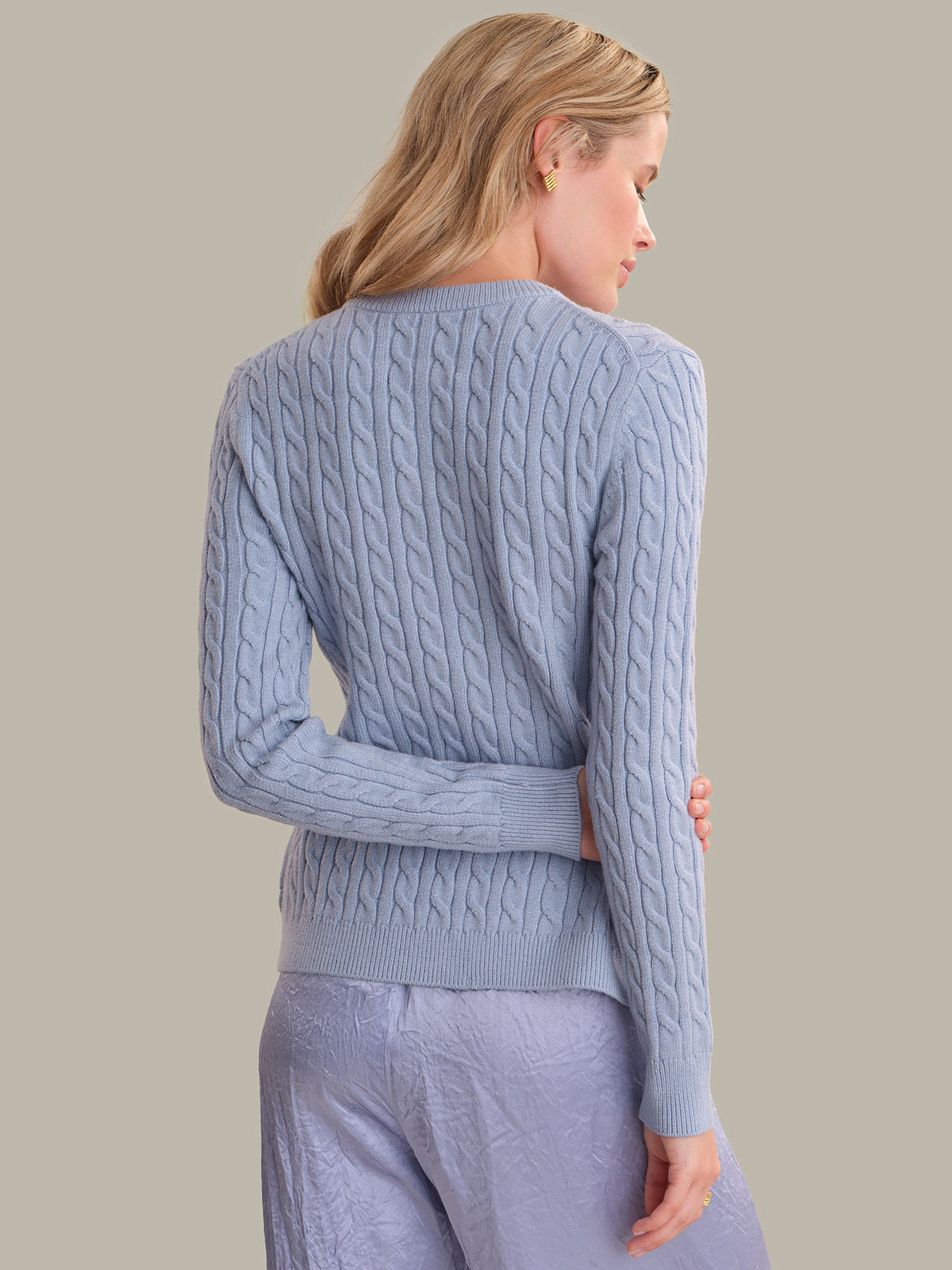 A woman shown from the back wearing a light blue cable-knit sweater and matching light blue pants against a plain beige studio background.