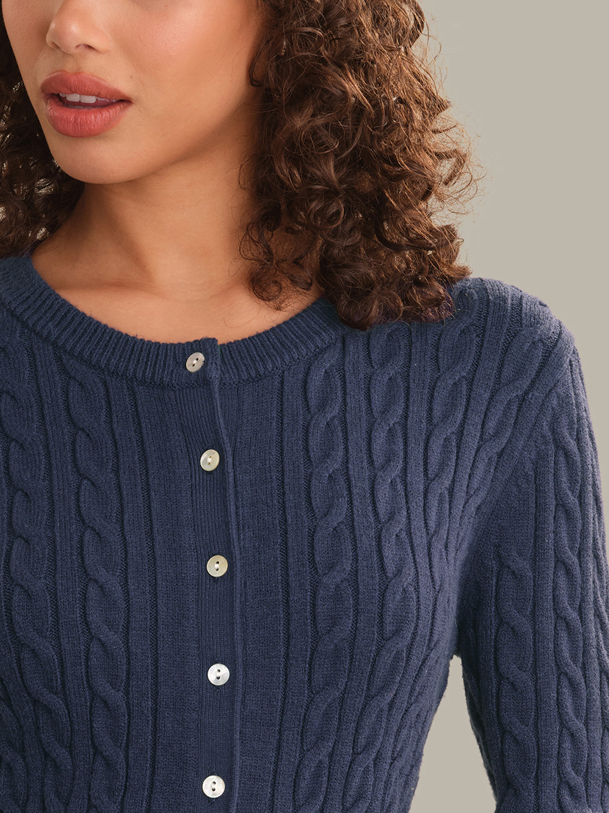 Close-up of a woman wearing a navy blue cable-knit cardigan sweater with a buttoned neckline.