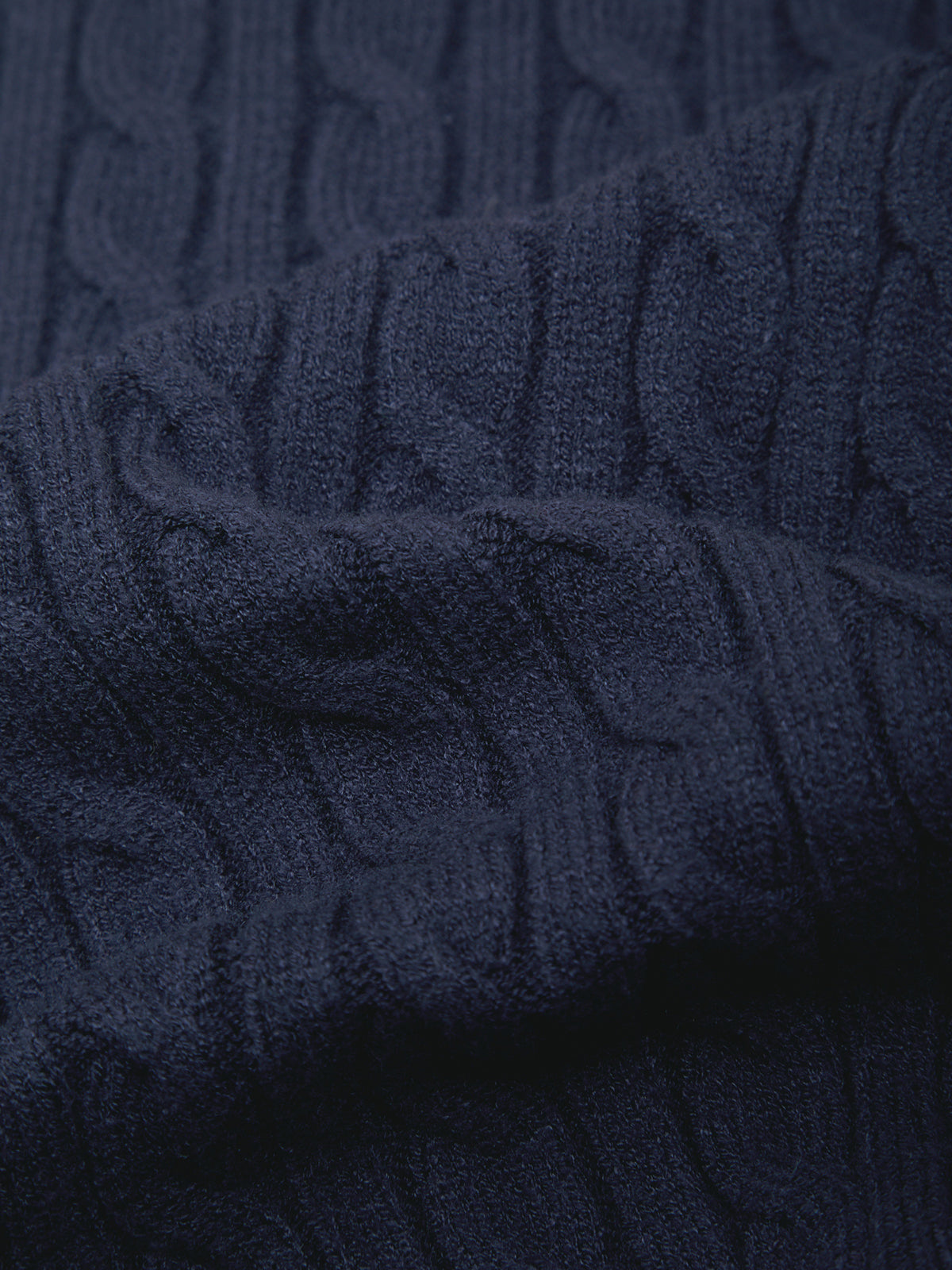Close-up of a dark navy blue cable-knit fabric texture with soft folds and shadows.