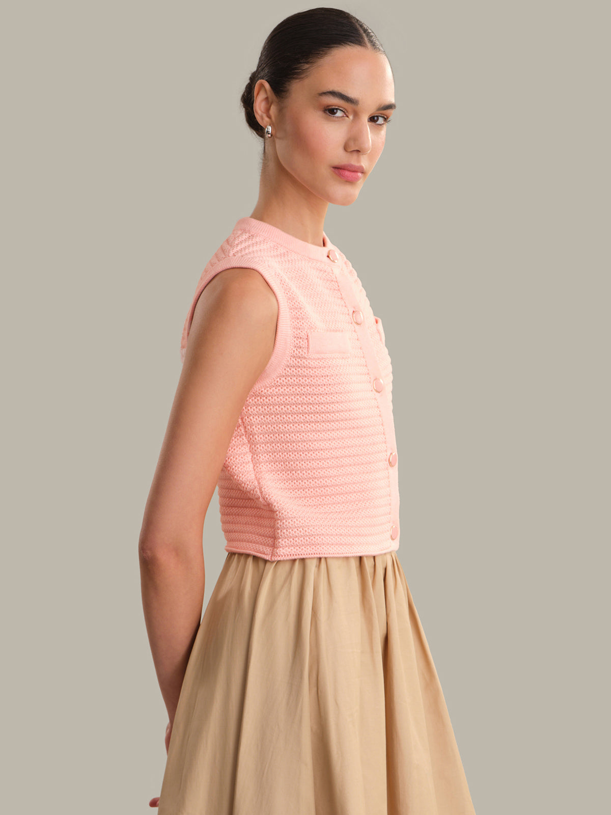 Woman wearing a pink sleeveless top and beige skirt against a gray background