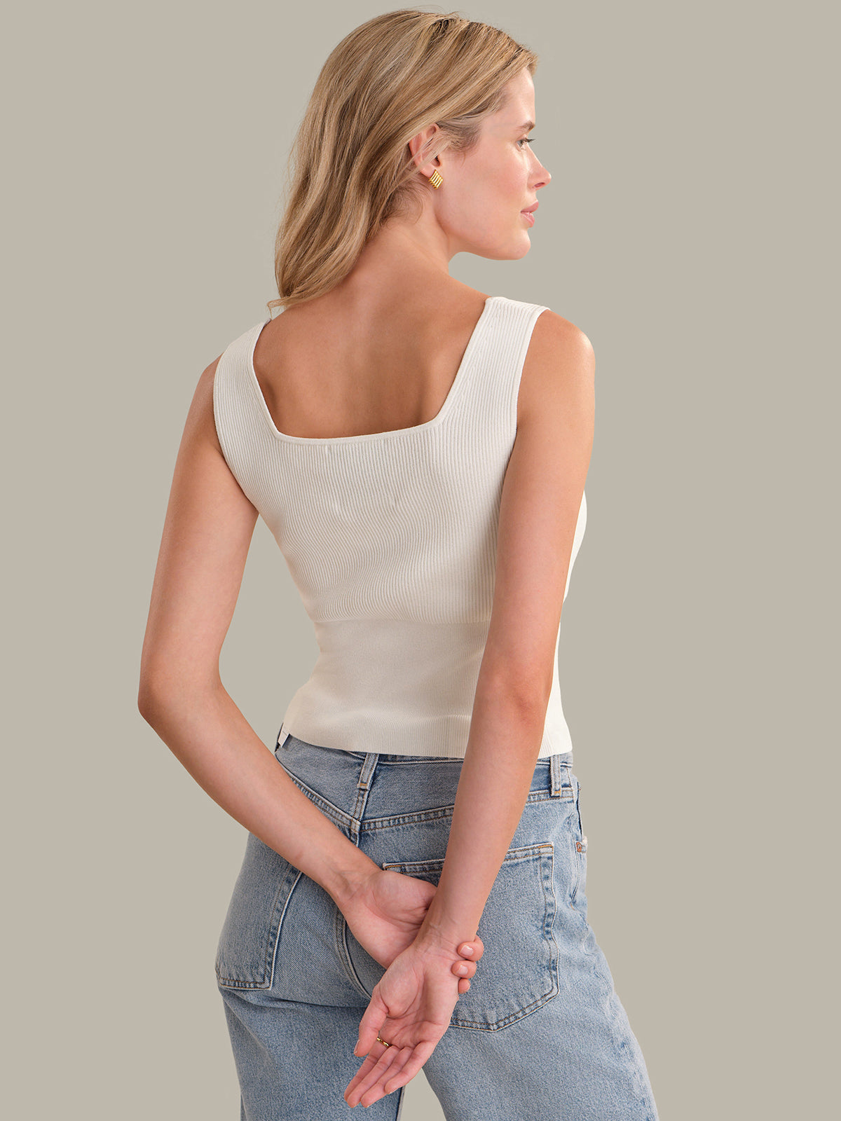 Woman wearing a white sleeveless top and blue jeans on a plain background