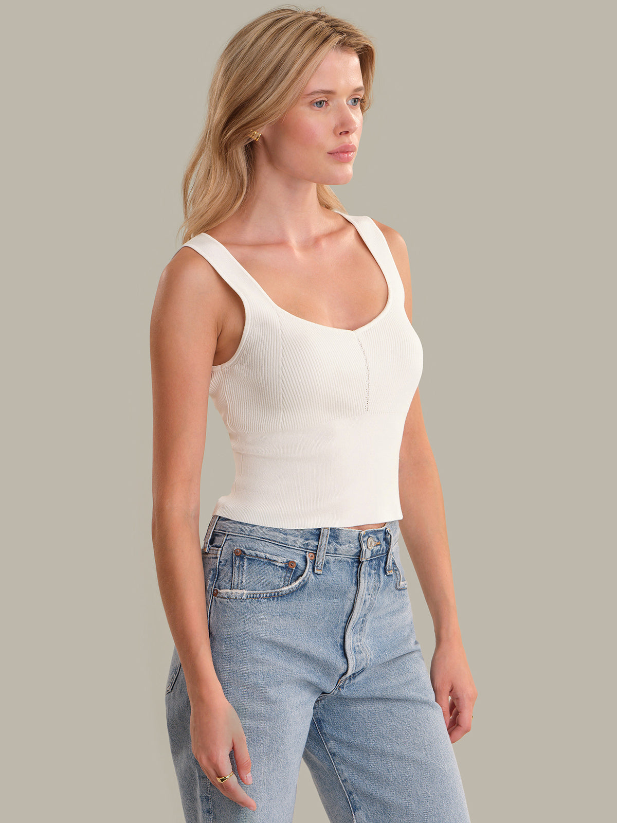 Woman wearing a white tank top and blue jeans against a plain background