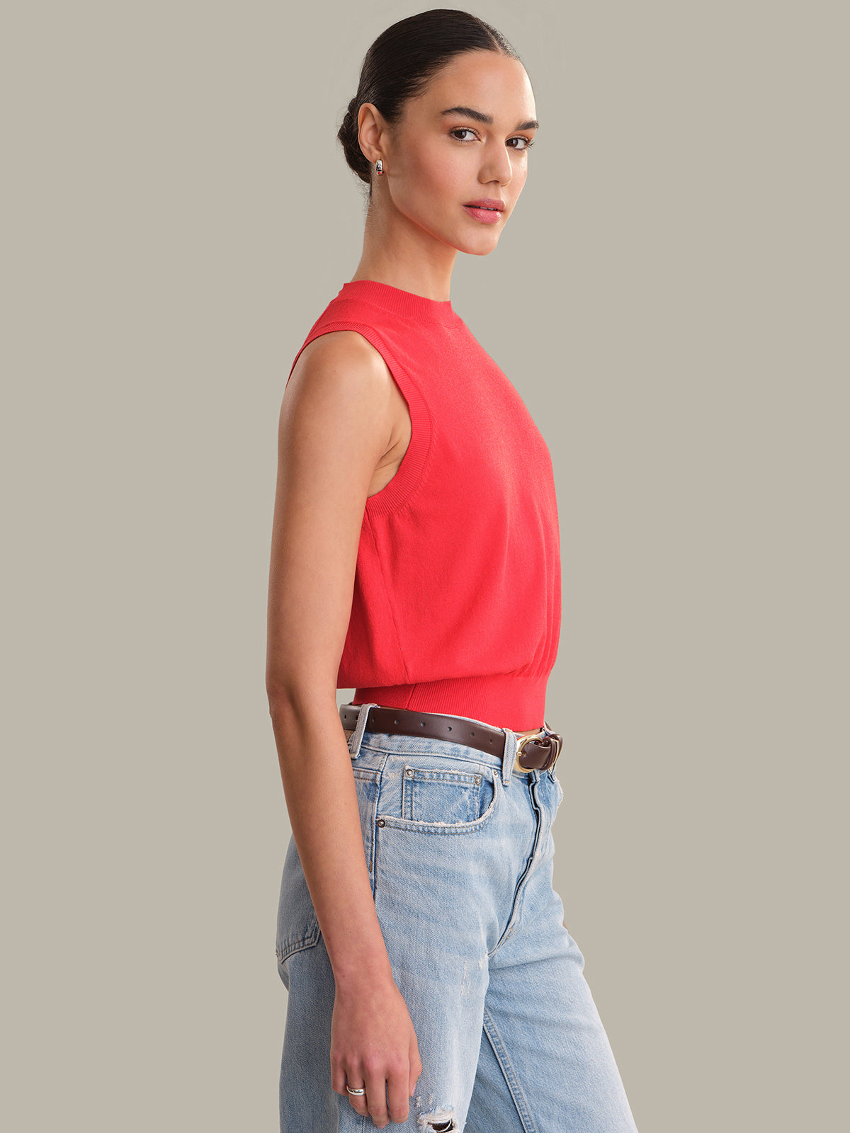 Woman wearing a red sleeveless top and light blue jeans on a gray background