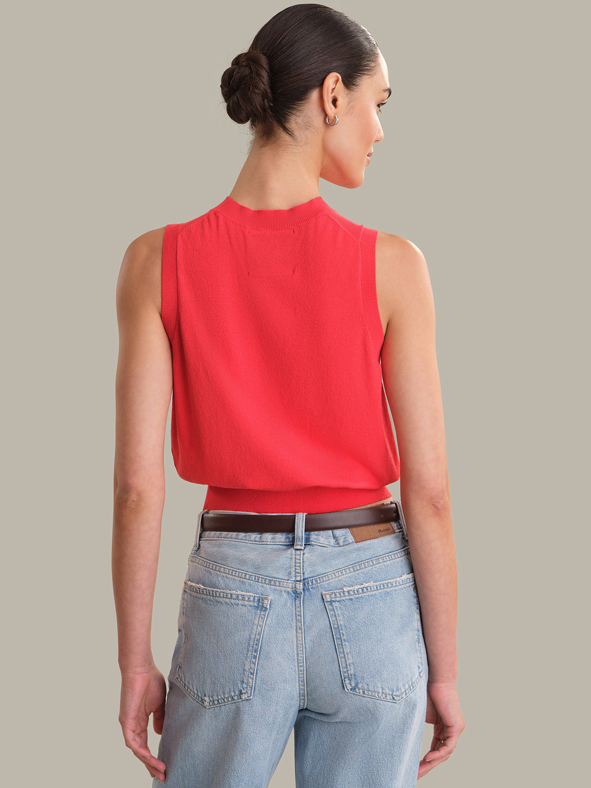 Woman wearing a red sleeveless top and light blue jeans on a plain background
